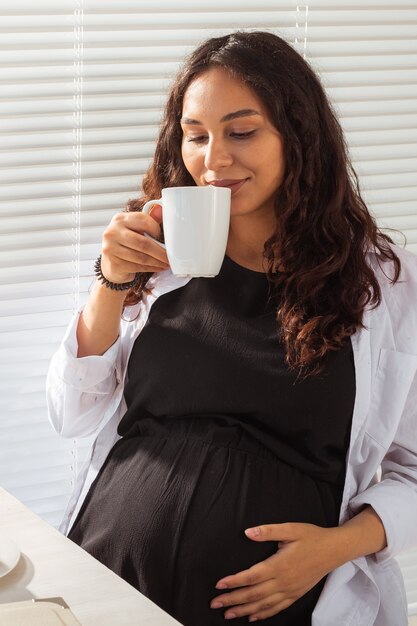 Mulher bonita jovem grávida feliz bebe chá durante o café da manhã. conceito de manhã agradável e atitude positiva durante a gravidez