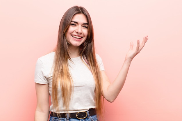 Mulher bonita jovem, sentindo-se feliz, surpreso e alegre, sorrindo com atitude positiva, percebendo uma solução ou idéia contra a parede rosa