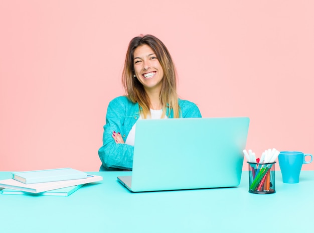 Mulher bonita jovem trabalhando com um laptop, parecendo um empreendedor feliz, orgulhoso e satisfeito, sorrindo com os braços cruzados