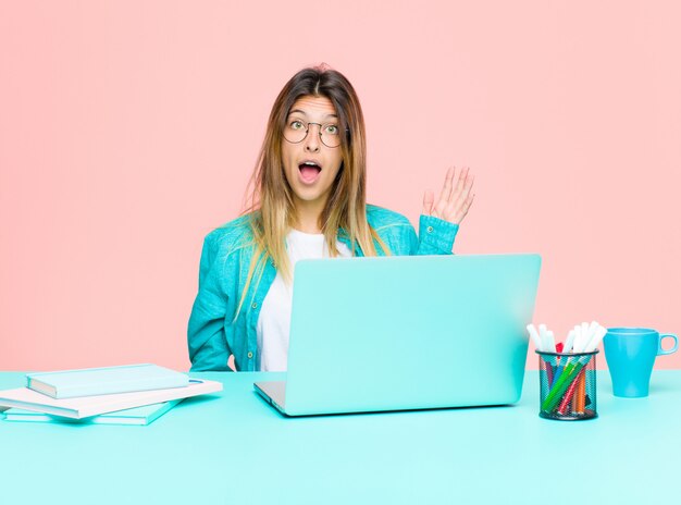 Mulher bonita jovem trabalhando com um laptop se sentindo feliz, surpreso e alegre, sorrindo com atitude positiva, percebendo uma solução ou idéia