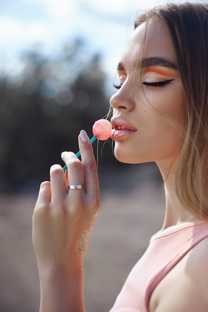 Foto mulher bonita lambendo um close-up de pirulito. sombras vermelhas nos olhos de uma menina, maquiagem profissional, cosméticos naturais