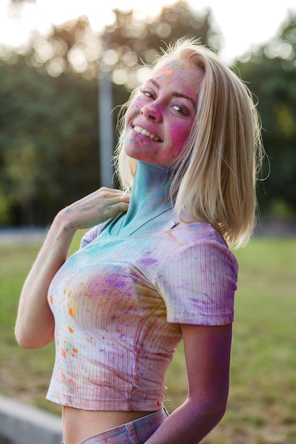 Mulher bonita loira em uma camiseta branca e shorts jeans azul coberto com tinta colorida seca holi, gulal