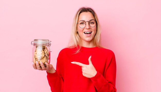 Mulher bonita loira olhando animada e surpresa apontando para o conceito de biscoitos laterais