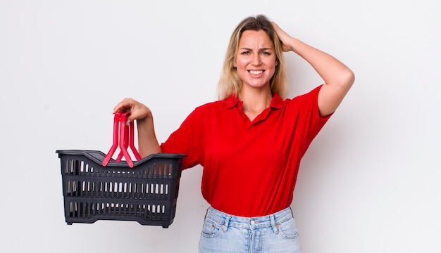 Mulher bonita loira se sentindo estressada, ansiosa ou assustada com as mãos na cabeça conceito de cesta de compras