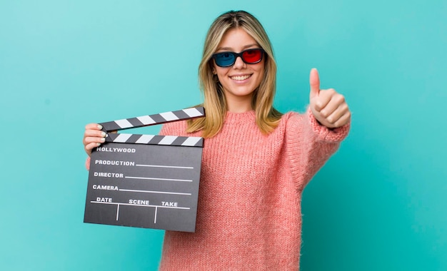 Mulher bonita loira se sentindo orgulhosa sorrindo positivamente com polegares para cima o conceito de cinema