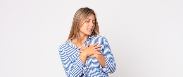 Mulher bonita loira se sentindo preocupada, esperançosa e religiosa, rezando fielmente com as palmas das mãos pressionadas, implorando perdão