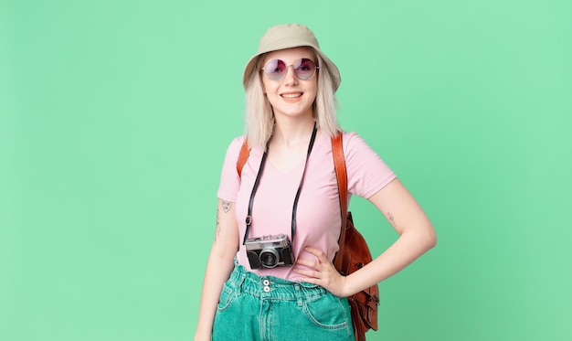 Mulher bonita loira sorrindo alegremente com uma mão no quadril e conceito de verão confiante