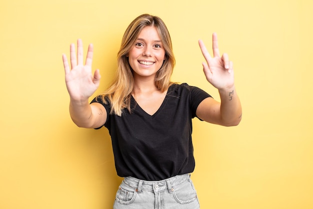 Mulher bonita loira sorrindo e parecendo amigável, mostrando o número oito ou oitavo com a mão para a frente, em contagem regressiva