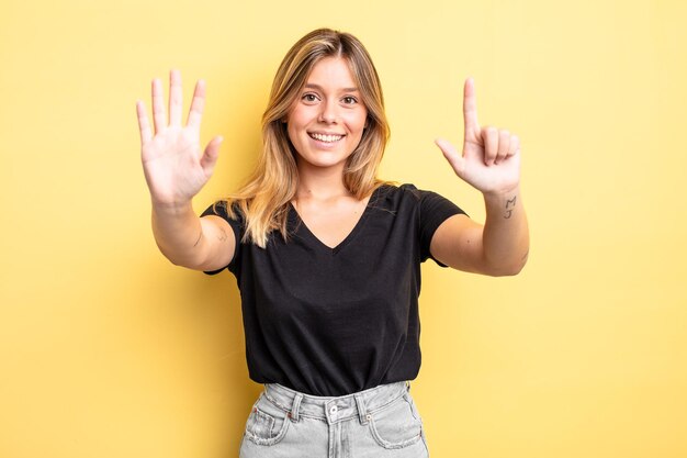 Mulher bonita loira sorrindo e parecendo amigável, mostrando o número sete ou sétimo com a mão para a frente, em contagem regressiva