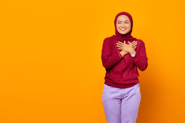 Mulher bonita mantém as mãos no sorriso do coração positivamente sobre fundo amarelo