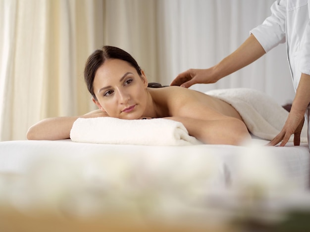 Mulher bonita morena, desfrutando de tratamento com pedras quentes no salão spa. Conceito de beleza.