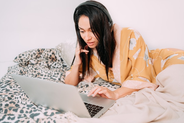 Mulher bonita na cama com fones de ouvido e computador