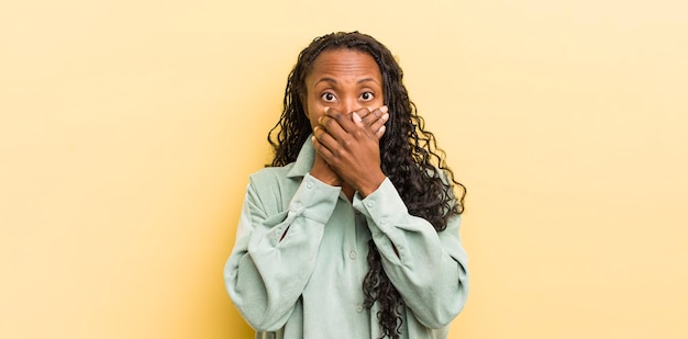 Mulher bonita negra cobrindo a boca com as mãos com uma expressão surpresa chocada mantendo um segredo ou dizendo oops