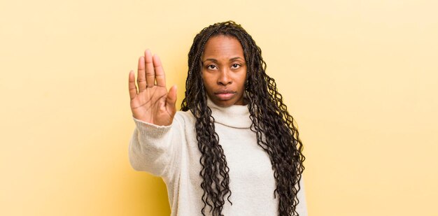 Mulher bonita negra, olhando séria, descontente e irritada, mostrando a palma da mão aberta fazendo gesto de parada