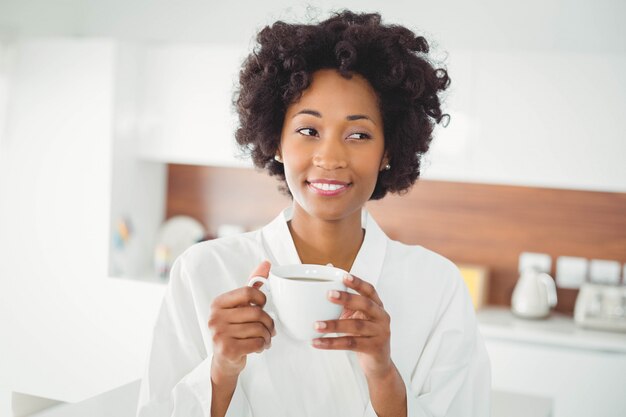 Mulher bonita no roupão de banho tomando café na cozinha em casa