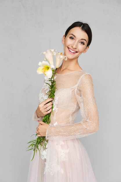 Mulher bonita no vestido transparente pálido com laço posando com flores na mão