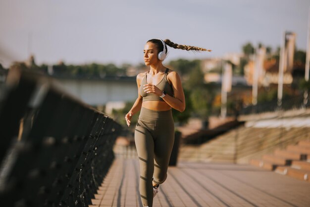 Mulher bonita nova ativa que corre no passeio ao longo do beira-rio