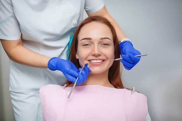 Mulher bonita nova com os dentes brancos bonitos que sentam-se em uma cadeira dental.