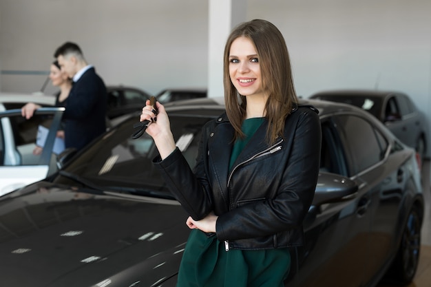 Mulher bonita ou vendedor de carros segurando a chave remota de um carro novo em um showroom