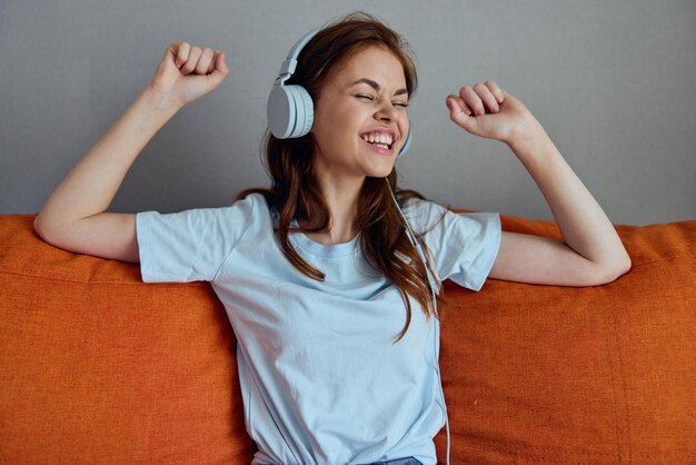 Mulher bonita ouvindo música com fones de ouvido nos apartamentos do sofá laranja