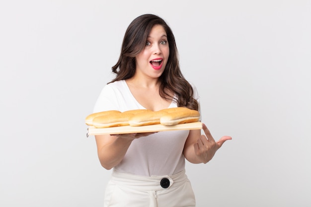 Foto mulher bonita parecendo animada e surpresa, apontando para o lado e segurando uma bandeja de pão