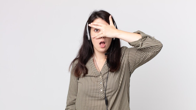 Mulher bonita parecendo chocada, assustada ou apavorada, cobrindo o rosto com a mão. agente assistente com fone de ouvido