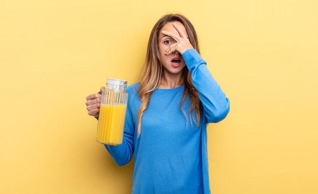 Mulher bonita parecendo chocada, assustada ou aterrorizada, cobrindo o rosto com o conceito de suco de laranja de mão