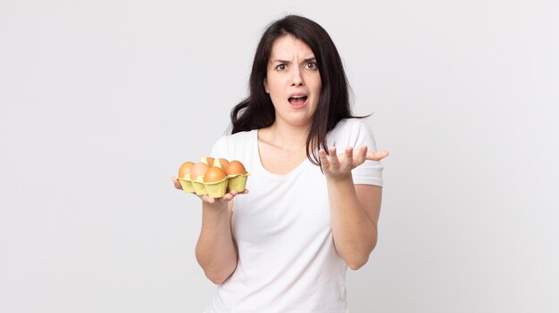 Mulher bonita parecendo desesperada, frustrada e estressada segurando uma caixa de ovos