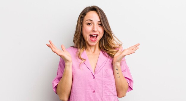 Mulher bonita parecendo feliz e animada chocada com uma surpresa inesperada com as duas mãos abertas ao lado do rosto