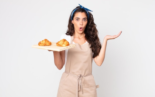 Mulher bonita parecendo surpresa e chocada, com o queixo caído segurando um objeto e uma bandeja de croissants