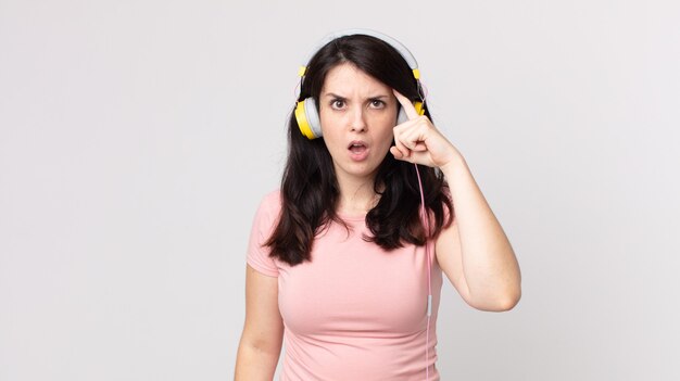 Mulher bonita parecendo surpresa, percebendo um novo pensamento, ideia ou conceito ouvindo música com fones de ouvido