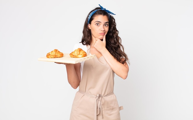 Mulher bonita pensando, se sentindo em dúvida e confusa e segurando uma bandeja de croissants