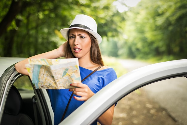 Mulher bonita perdida confusa em pé encostado no carro na floresta e preocupado olhando um mapa.