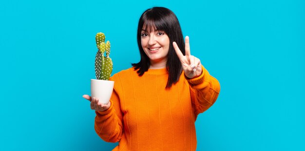 Mulher bonita plus size sorrindo e parecendo feliz, despreocupada e positiva, gesticulando vitória ou paz com uma mão