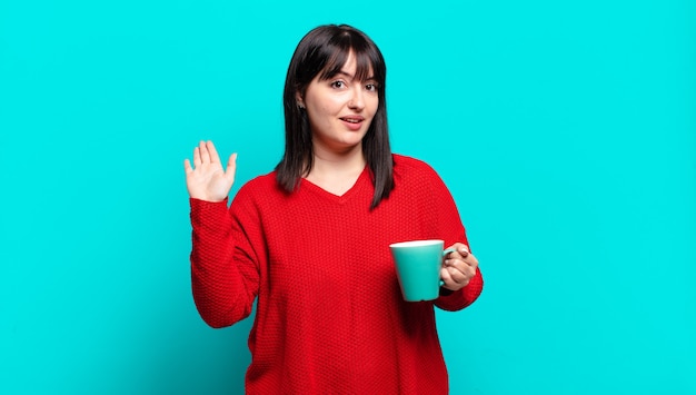 Mulher bonita plus size sorrindo feliz e alegre, acenando com a mão, dando as boas-vindas e cumprimentando você ou dizendo adeus