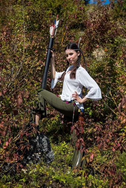 Mulher bonita posando com roupa e arma tradicionais como uma guerreira indígena ao ar livre