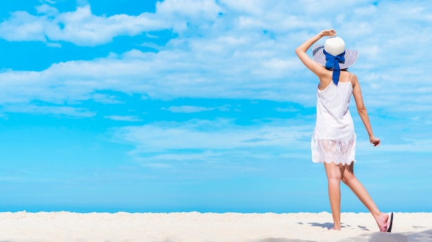 Mulher bonita que anda na praia com céu azul. Férias de verão feliz.