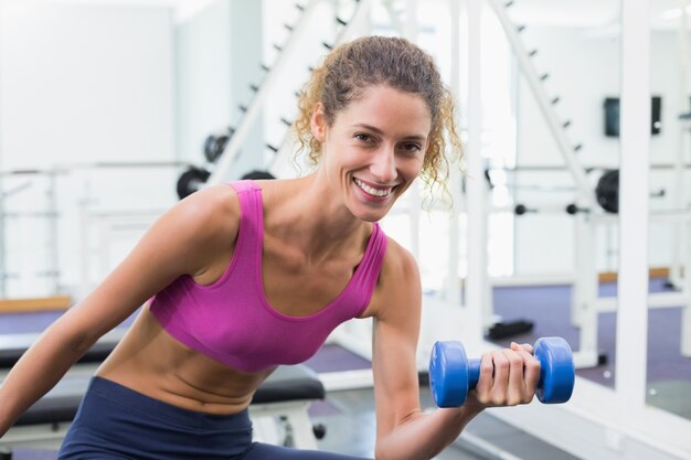 Mulher bonita que levanta dumbbell azul sentada no banco