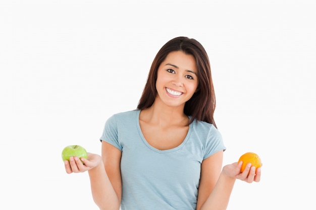 Mulher bonita que segura uma maçã e uma laranja