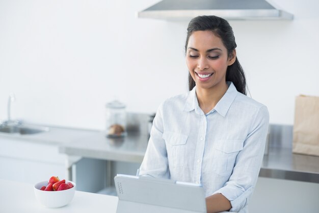 Mulher bonita que trabalha em seu tablet em sua cozinha