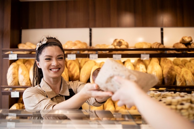 Mulher bonita que trabalha na padaria e vende pastelaria saborosa fresca para o cliente