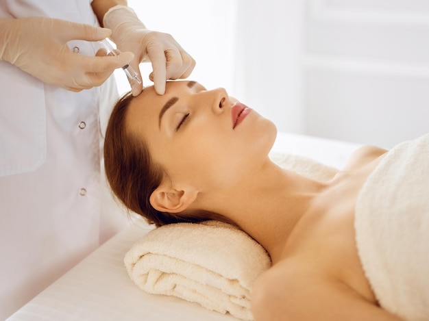 Mulher bonita recebendo injeções de beleza com os olhos fechados. Mãos de médico esteticista fazendo procedimento de beleza no rosto feminino com seringa. Conceito de medicina e cirurgia cosmética.