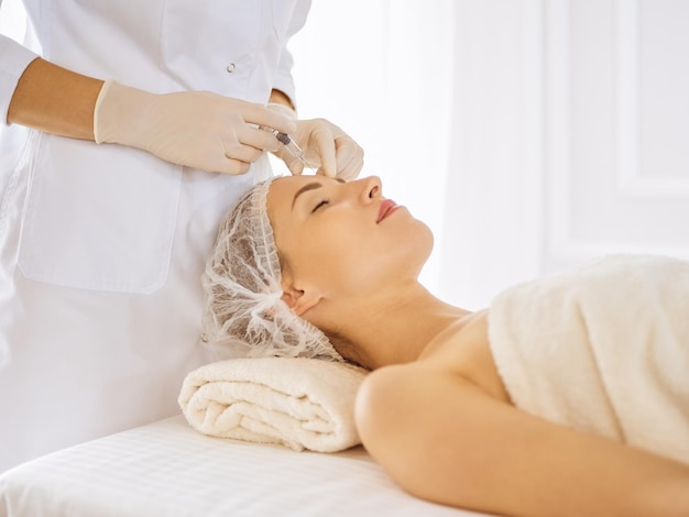Mulher bonita recebendo injeções de beleza com os olhos fechados. Mãos de médico esteticista fazendo procedimento de beleza no rosto feminino com seringa. Conceito de medicina e cirurgia estética