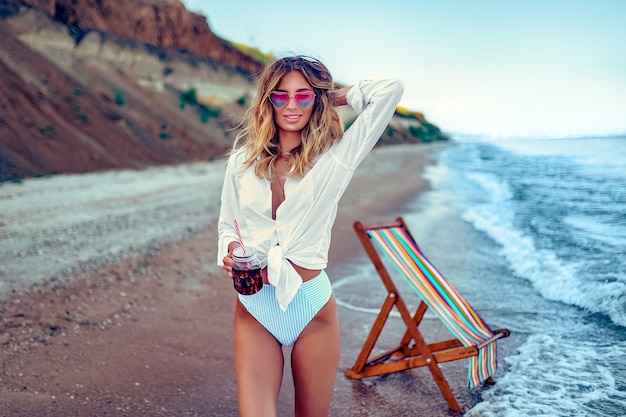 Foto mulher bonita relaxante na praia e bebe coctail. conceito de férias de verão