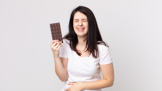 Mulher bonita rindo alto de uma piada hilária e segurando uma barra de chocolate