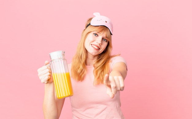 Mulher bonita ruiva de pijama e segurando um suco de laranja. conceito de café da manhã saudável