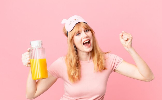 Mulher bonita ruiva de pijama e segurando um suco de laranja. conceito de café da manhã saudável