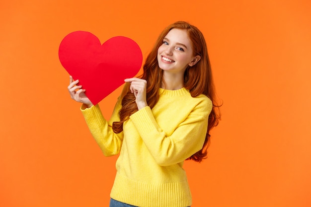 Mulher bonita ruiva romântica e macia na camisola amarela segurando coração grande