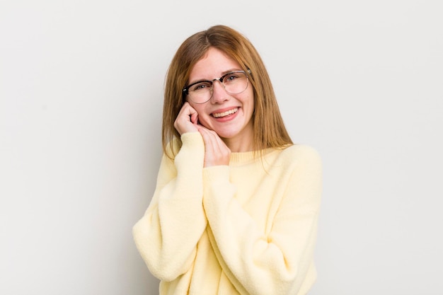 Foto mulher bonita ruiva se sentindo apaixonada e bonita adorável e feliz sorrindo romanticamente com as mãos ao lado do rosto