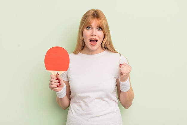 Mulher bonita ruiva se sentindo chocada rindo e comemorando o conceito de ping pong de sucesso